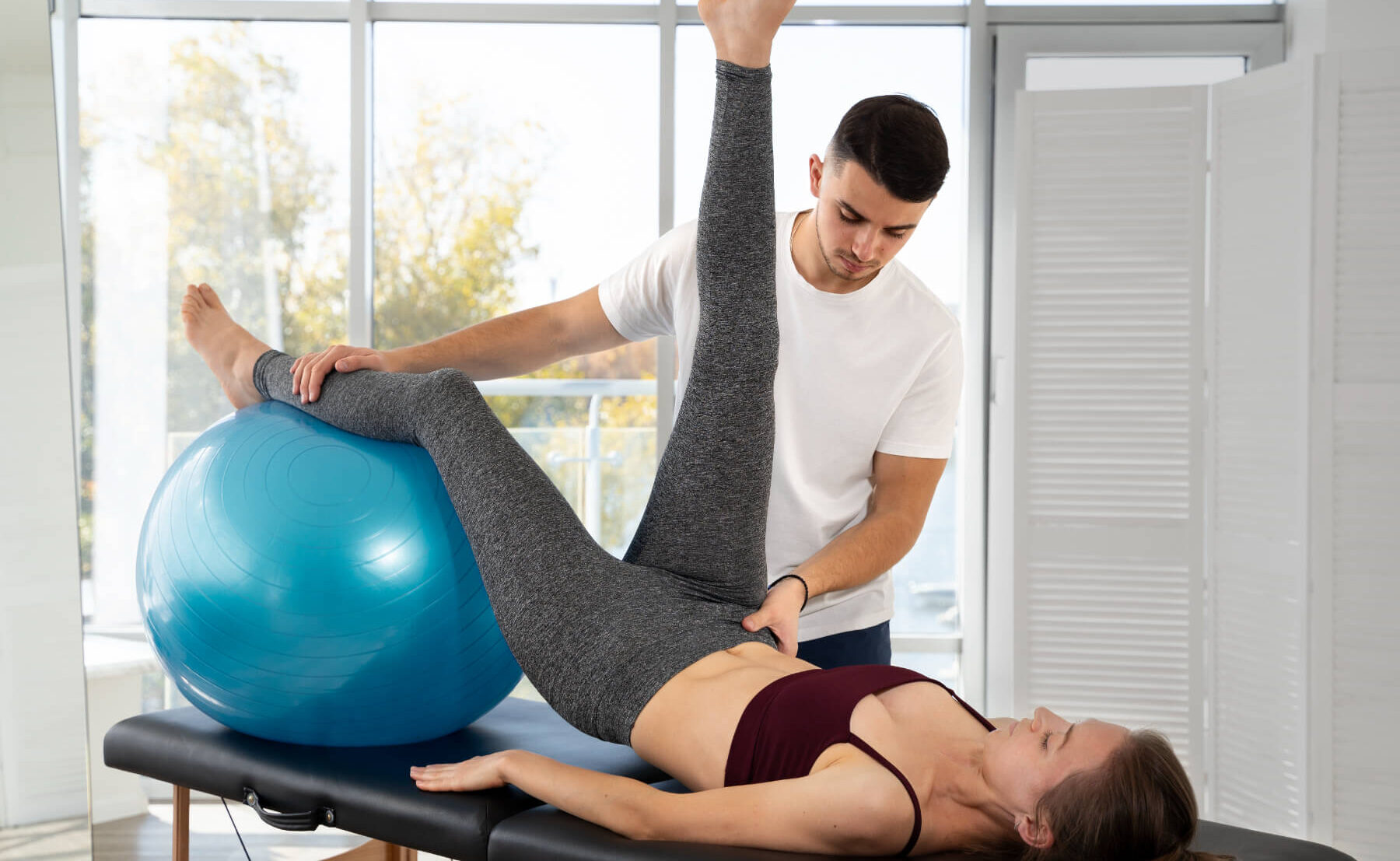 Therapeut hilf Patientin bei einer Übung für Beine und Hüfte mit dem Gymnastikball