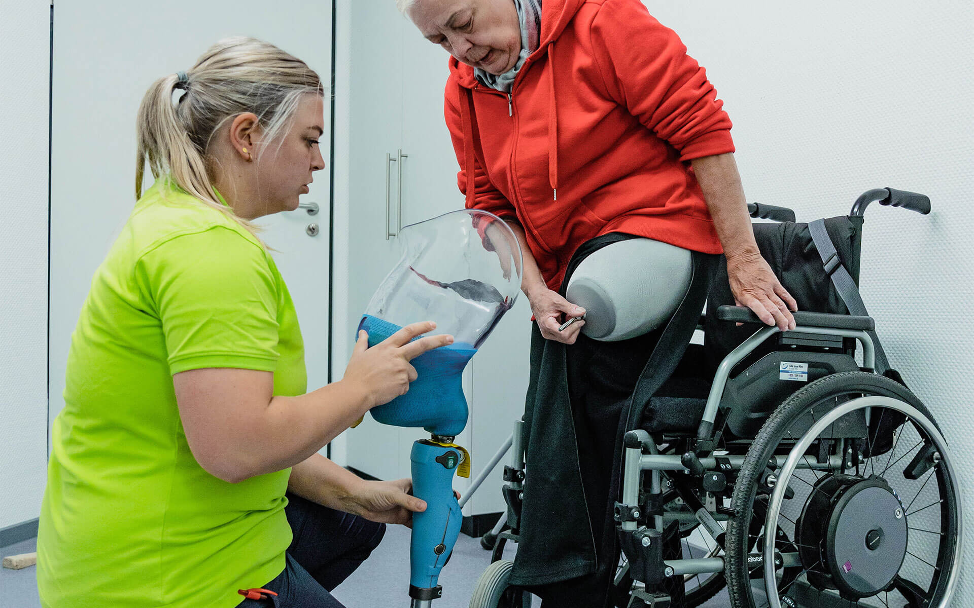 Pflegerin hilft einer Patientin ihre Beinprothese anzulegen.