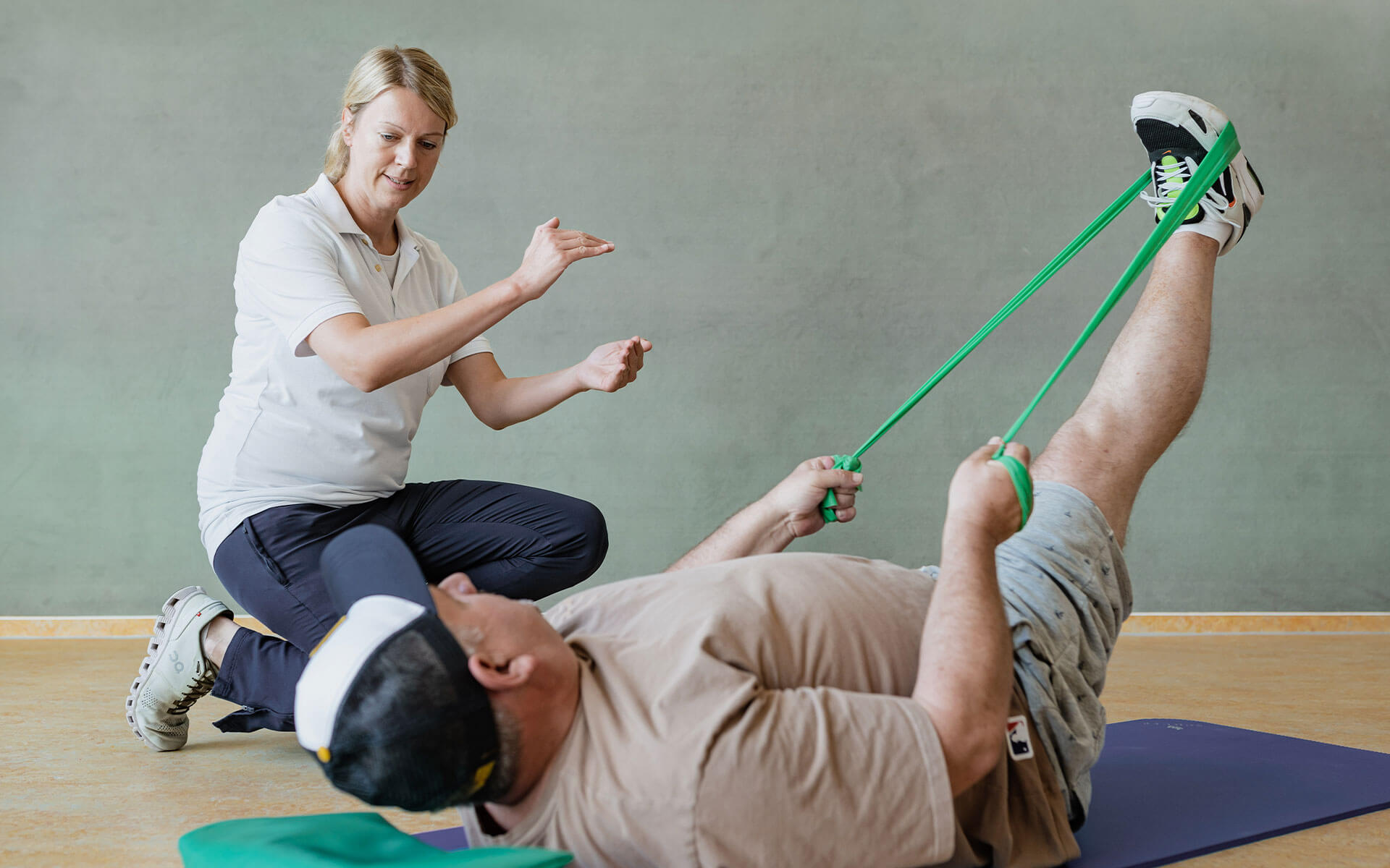 Mann in therapeutischer Behandlung trainiert / streckt sein Bein mit Theraband.