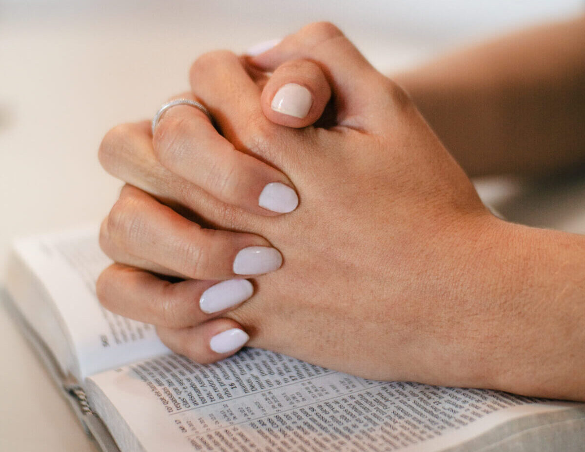 Nahaufnahme von zwei betenden Händen, die auf der Bibel liegen